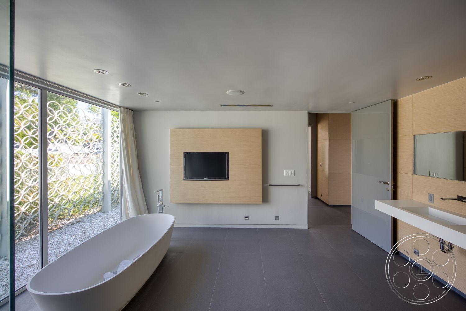 Modern 525 - wall-mounted television, wood cabinetry, modern bathroom, large glass windows, sliding glass door, textured wall paneling, gray stone flooring, minimalist wall treatment, freestanding soaking tub, floating vanity countertop, integrated LED lighting
