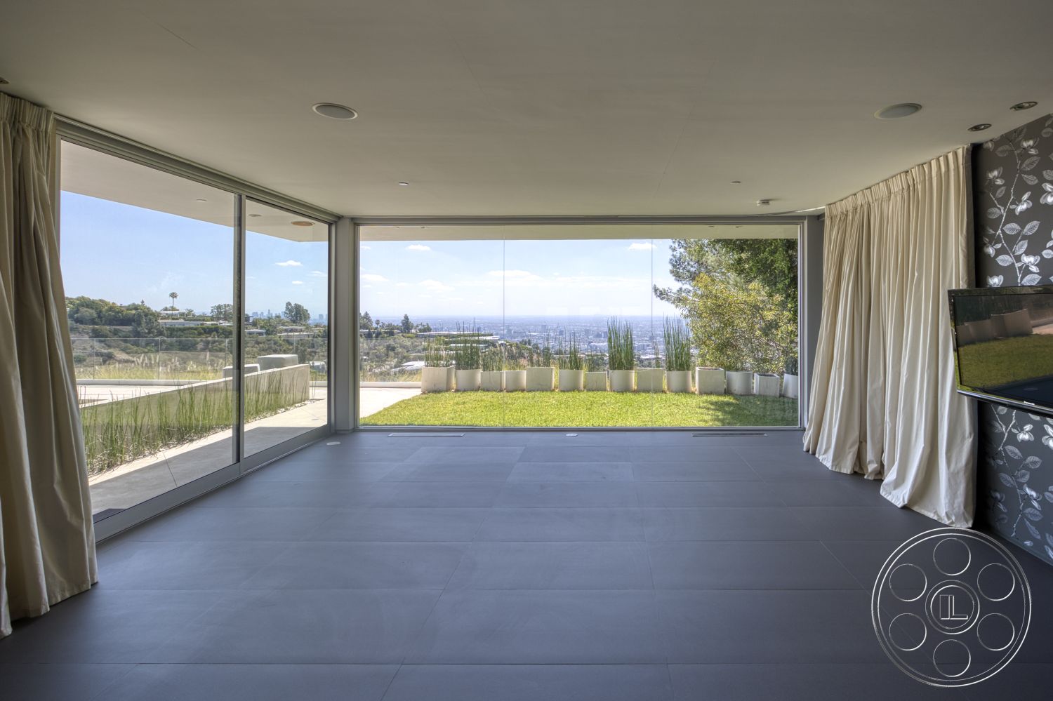 Modern 525 - minimalist design, large glass sliding doors, open floor plan, floor-to-ceiling windows, modern architectural style, elevated hillside location, green lawn view, neutral colored walls, curtains with floral pattern, smooth ceramic tile flooring