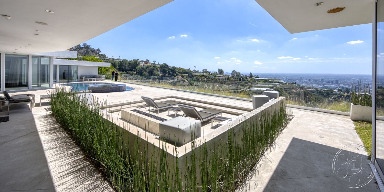 Modern 525 - exterior, white stucco walls, minimalist design, rectangular swimming pool, outdoor living space, panoramic city view, hillside location, modern lounge chairs, flat roof design, floor-to-ceiling glass windows, concrete patio floor, landscaped garden borders, sunny weather setting