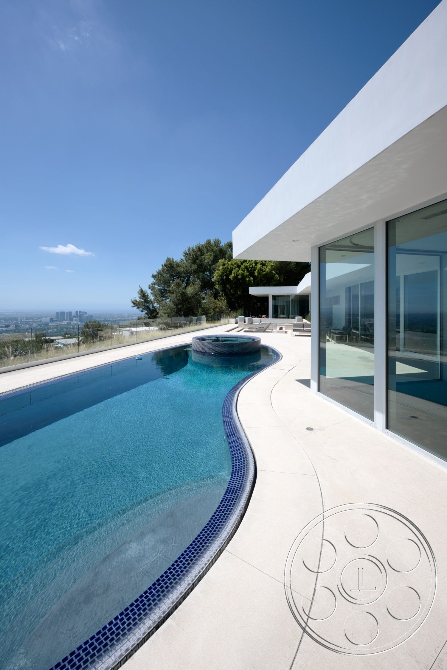 Modern 525 - exterior, large glass windows, rectangular swimming pool, outdoor lounge area, infinity pool, concrete pool border, minimalist architectural style, landscaped hillside setting, smooth concrete patio floor, tile pool coping, blue mosaic tile trim, cantilevered house design