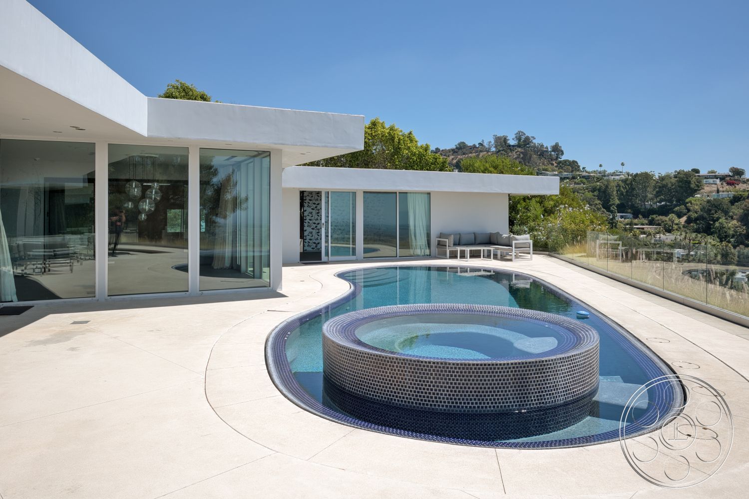 Modern 525 - exterior, flat roof, concrete pathway, infinity pool, curved pool shape, open floor plan design, modern outdoor seating area, glass floor-to-ceiling windows, concrete pool patio, white stucco exterior walls, surrounding hillside landscaping, hexagonal mosaic pool tiles