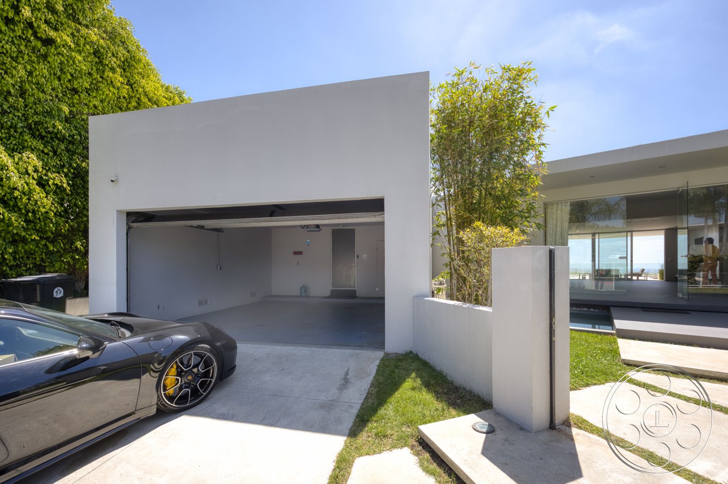 Modern 525 - exterior, flat roof, minimalist design elements, large glass windows, concrete driveway, stucco walls, outdoor pathway, contemporary architectural style, landscaped garden area, concrete garage floor, double garage door, greenery surrounding property, slab stone pathway, modern home entry, open space exterior layout