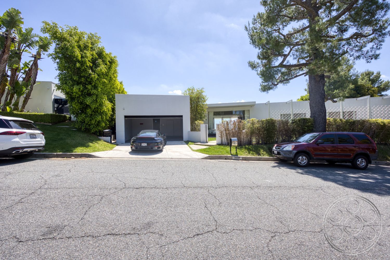 Modern 525 - exterior, low-maintenance landscaping, tree canopy, bushes and shrubs, paved walkway, modern architectural style, concrete driveway, residential setting, flat roof design, large glass entrance, concrete garage, front yard grass, curvilinear driveway