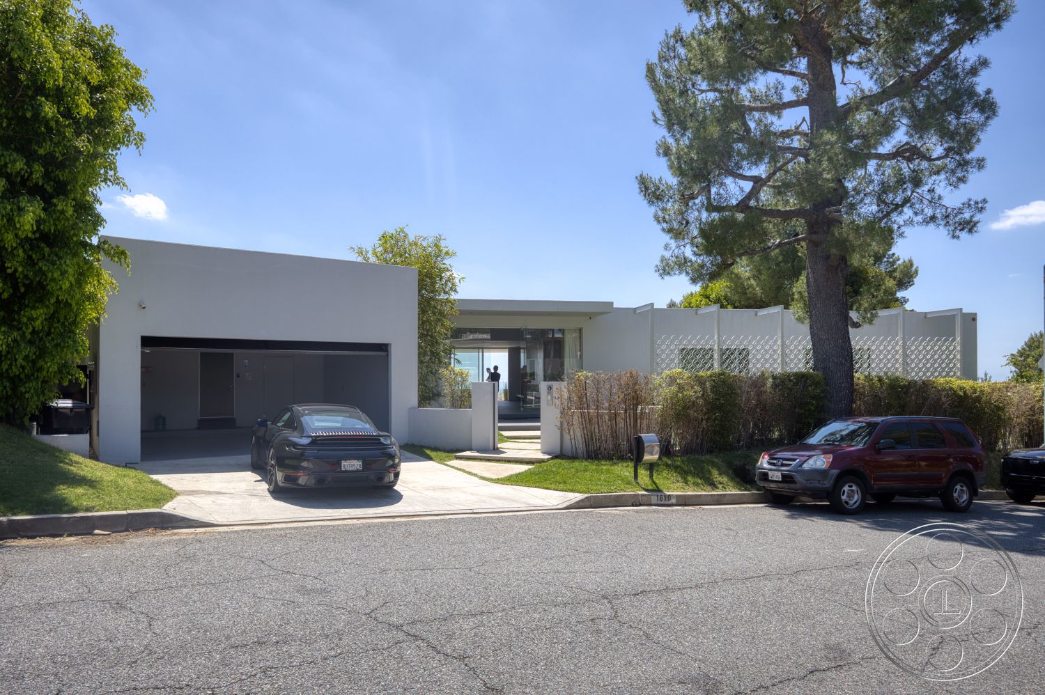 Modern 525 - large glass windows, landscaped front yard, single-story home, paved walkway, modern architectural style, concrete driveway, flat roof design, exterior concrete walls, metal mailbox, urban suburban setting, mixed greenery plants, oversized garage door, privacy screen fence, front patio area