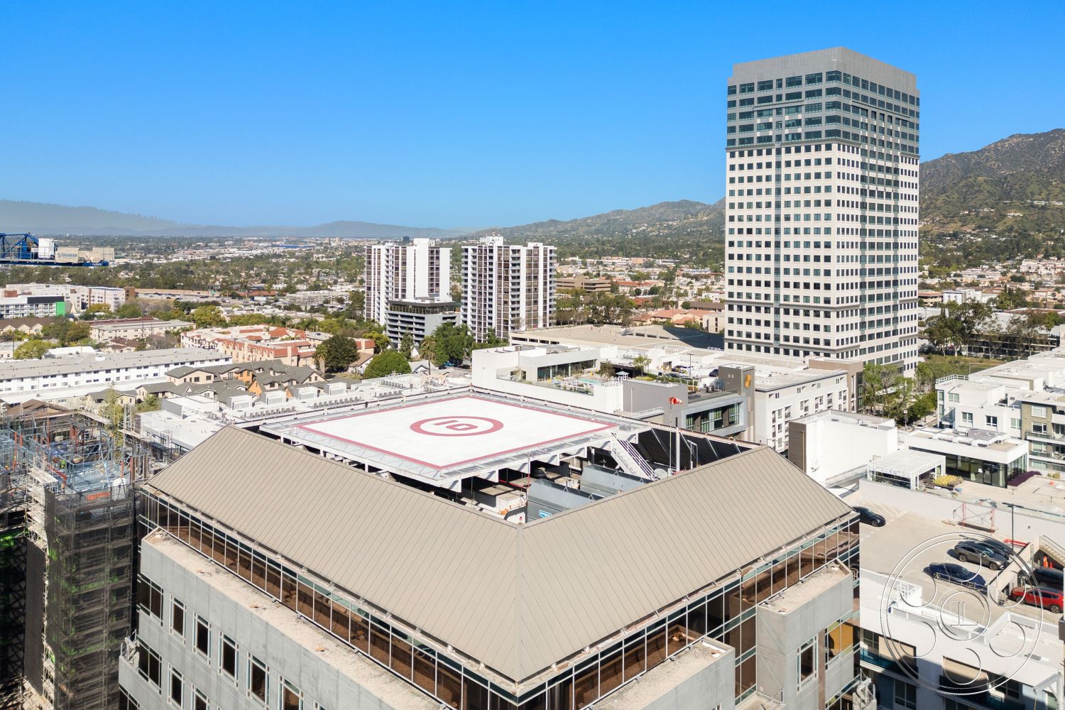 Rooftop-52 - exterior, glass facade, urban skyline view, steel framework, panoramic mountain view, concrete structural elements, surrounding urban setting, modern high-rise building, flat roof with helicopter landing pad, metal railing on rooftop, surrounding multi-story residential buildings