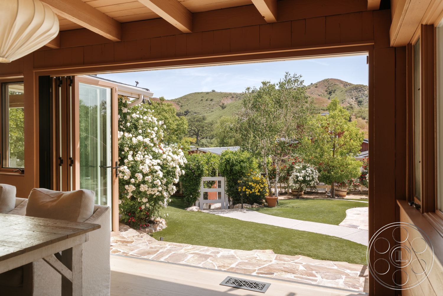 Modern-Farmhouse 20 - exterior, mountain view, wood beam ceiling, stone patio flooring, rustic farmhouse style, landscaped garden with flowering plants, integrated indoor-outdoor living space, folding glass doors, lawn with artificial grass
