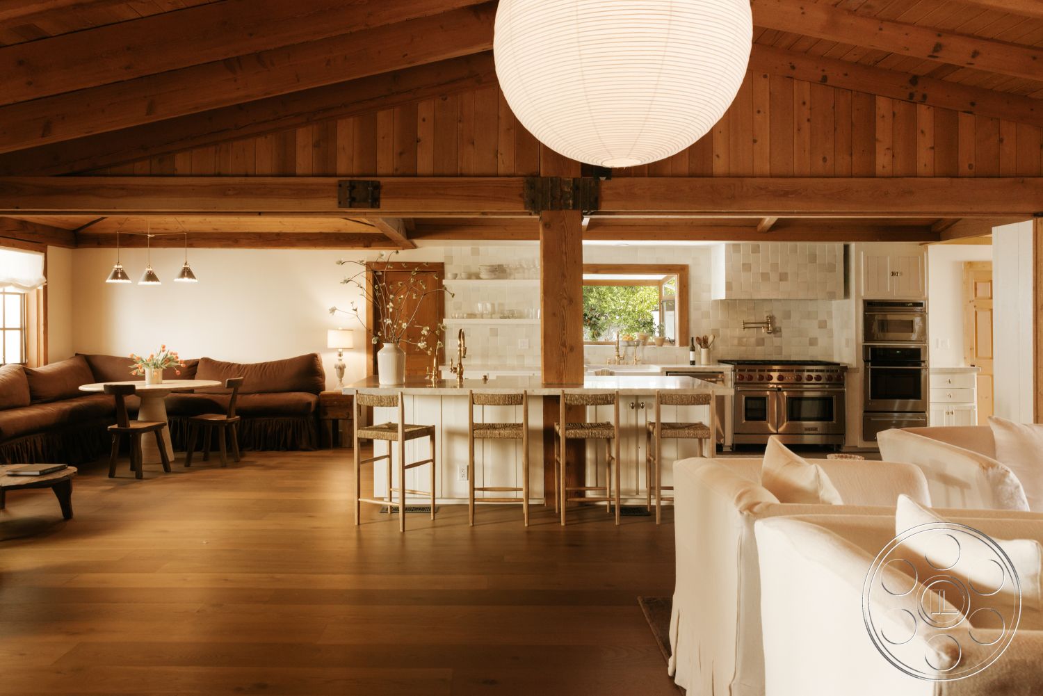 Modern-Farmhouse 20 - modern pendant lighting, exposed wood ceiling beams, stainless steel kitchen appliances, hardwood living room floors, built-in kitchen cabinets, white painted walls, open floor plan living area, large windows with natural light, cozy sectional sofa, stone kitchen backsplash, island kitchen with bar seating, dining area with round table