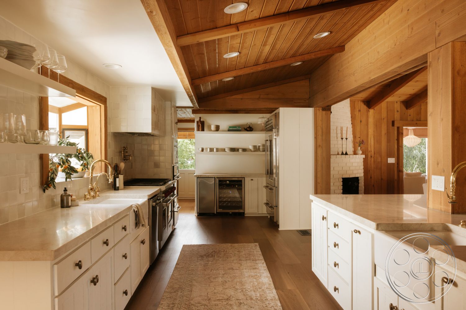 Modern-Farmhouse 20 - neutral color palette, decorative area rug, stainless steel appliances, open shelving, vaulted ceiling, marble countertop, natural light from windows, exposed brick fireplace wall, wood beam ceiling, hardwood kitchen floors, white subway tile backsplash, white shaker kitchen cabinets, industrial-style faucet, double-basin farmhouse sink