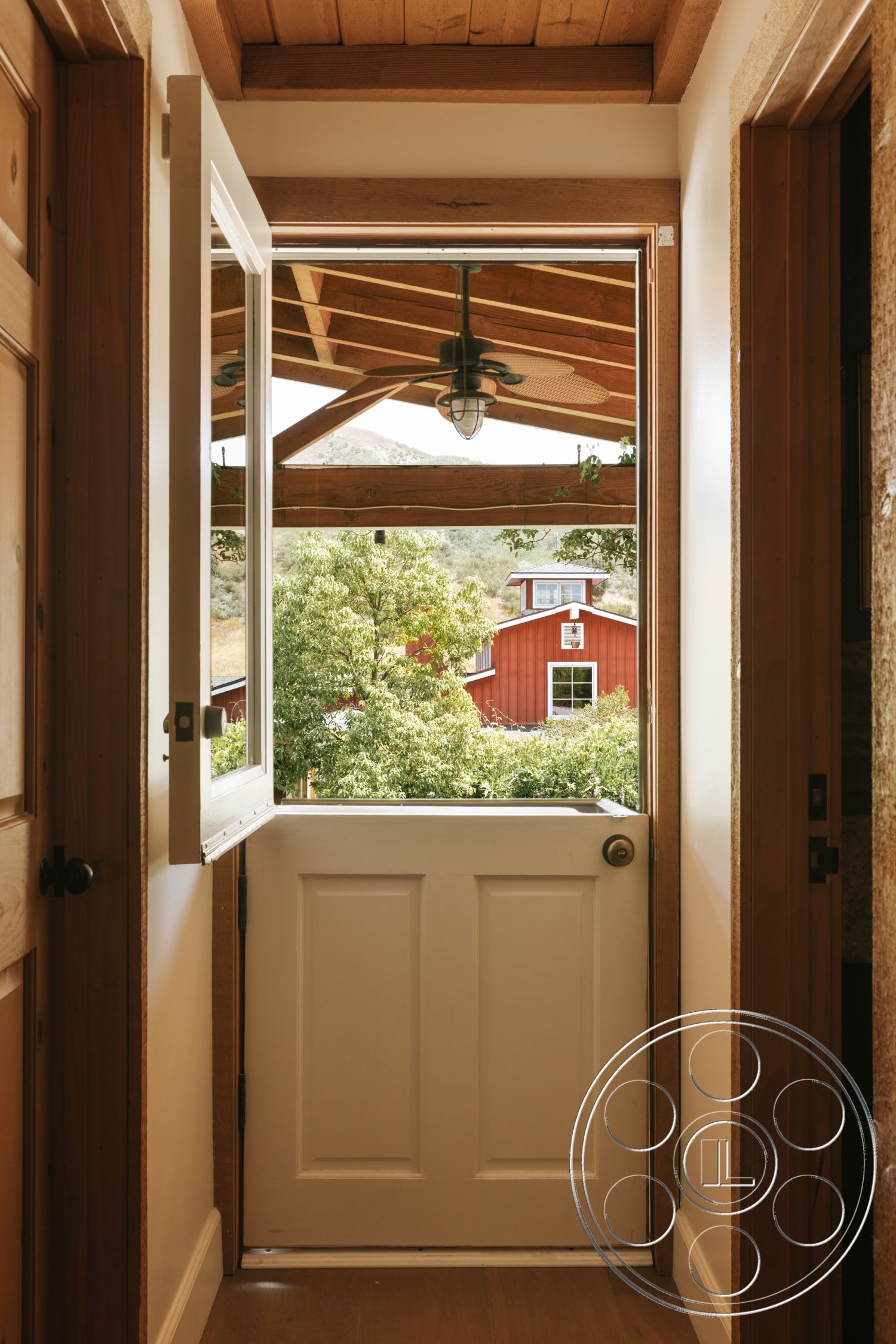 Modern-Farmhouse 20 - hardwood flooring, exposed wooden beams, interior hallway, wood beam ceiling, natural light entryway, rustic farmhouse style, white interior door, paneled wooden door frame, open door to outdoor view, panoramic view of surrounding trees