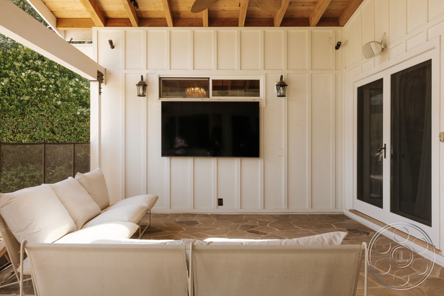 Modern-Farmhouse 20 - exterior, sliding glass doors, outdoor seating area, white shiplap walls, greenery backdrop, wood beam ceiling, stone patio flooring, flat-screen television wall mount, traditional outdoor lanterns