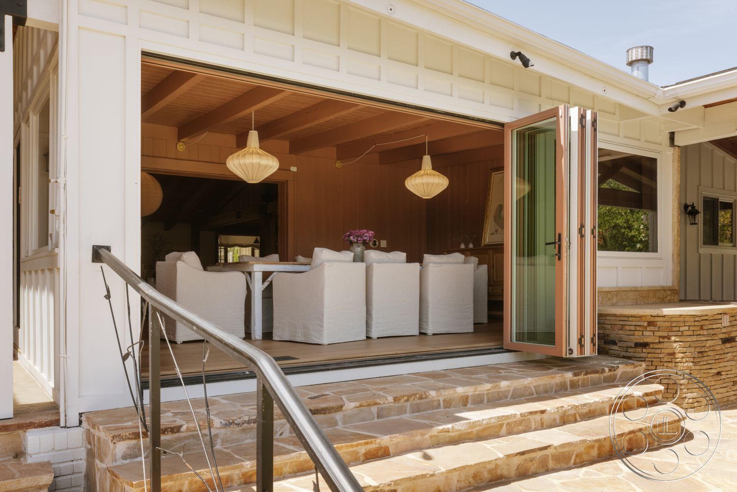 Modern-Farmhouse 20 - natural light, exterior, open floor plan, modern pendant lighting, concrete steps, landscaped backyard, textured wall paneling, exposed wood ceiling beams, stone patio flooring, wooden entrance door, dining room with white upholstered chairs, glass folding doors