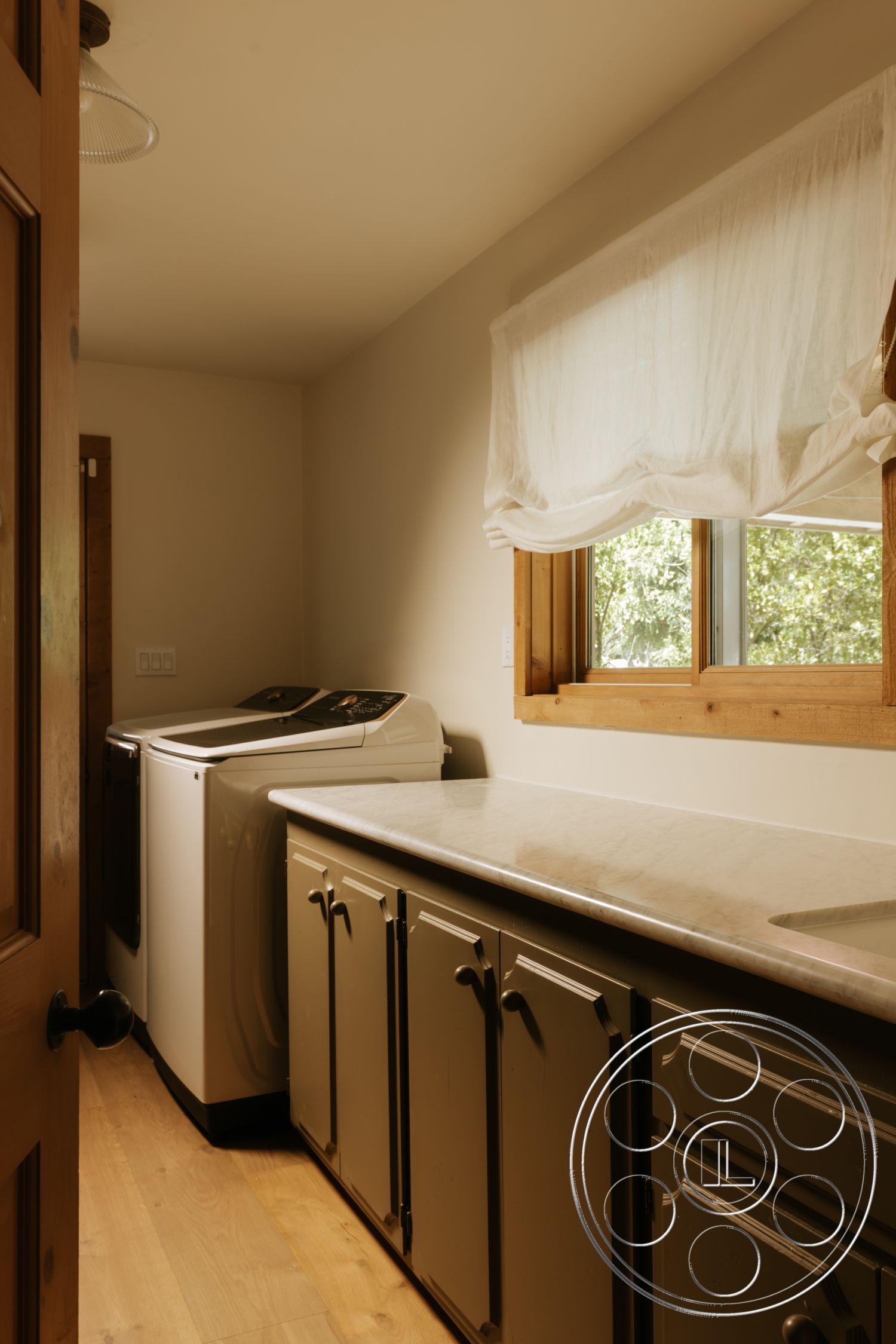 Modern-Farmhouse 20 - light wood flooring, earthy color palette, laminate countertop, interior laundry room, dark kitchen cabinetry, white washed wall treatment, single window with light fabric shade, modern washer and dryer, open spatial layout