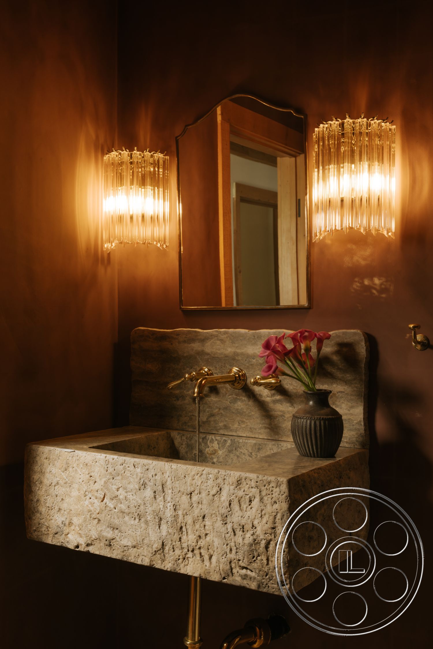 Modern-Farmhouse 20 - exterior, textured wall finish, stone sink, brass faucet fixtures, polished stone countertop, vintage-style wall sconces, framed mirror with decorative edges, dark brown wall treatment, natural light reflection, flower vase with fresh blooms
