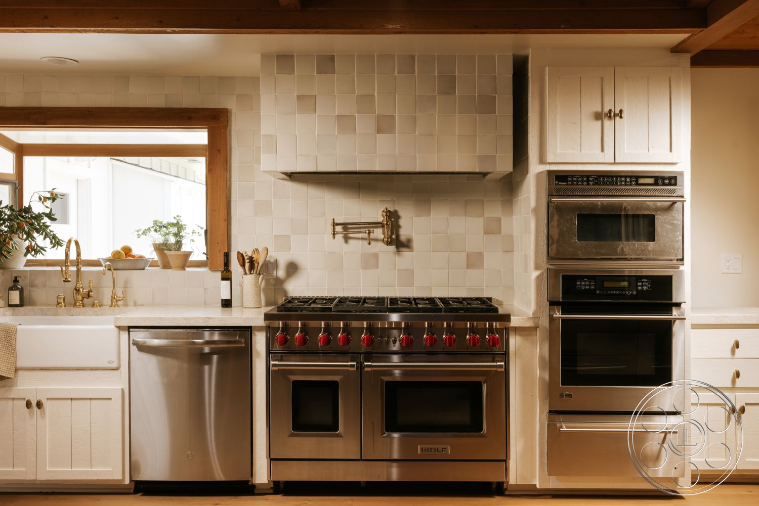 Modern-Farmhouse 20 - stainless steel appliances, warm natural light, exposed wood ceiling beams, open kitchen layout, stainless steel dishwasher, white subway tile backsplash, brass kitchen faucet, chefs kitchen, polished quartz countertops, white shaker-style kitchen cabinets, double basin farmhouse sink, built-in wall ovens, wood-framed window