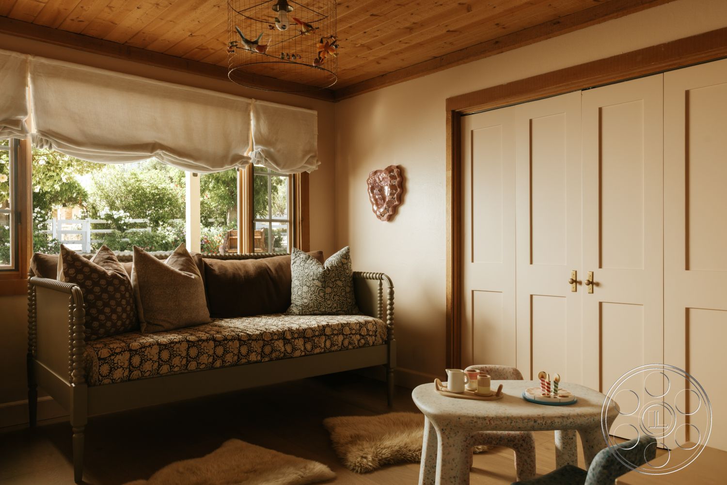 Modern-Farmhouse 20 - textured area rug, decorative wall art, textured plaster walls, exposed wooden ceiling beams, wood paneled ceiling, soft fabric cushions, beige painted walls, large wooden windows, button tufted daybed, simple round side table, light-colored closet doors