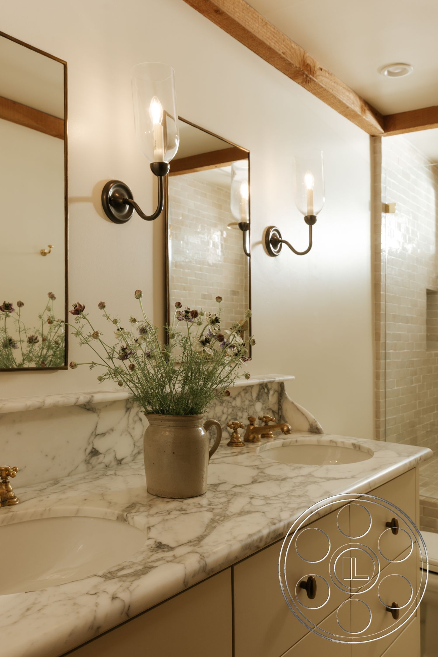 Modern-Farmhouse 20 - double sink vanity, marble countertop, gold faucet fixtures, neutral painted walls, wood beam ceiling, subway tile shower walls, marble bathroom vanity top, wall-mounted vanity lights, black metal sconces, bathroom mirrors, natural floral arrangements, textured shower enclosure