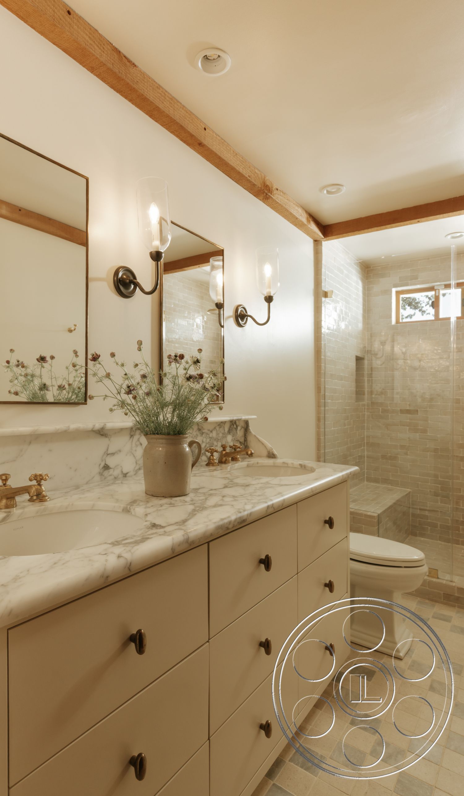 Modern-Farmhouse 20 - neutral color palette, glass light fixtures, rectangular mirrors, dual sink vanity, wood beam ceiling, marble bathroom countertop, built-in shower bench, stone shower walls, beige cabinetry, black cabinet handles, tile shower floor, polished tile bathroom flooring