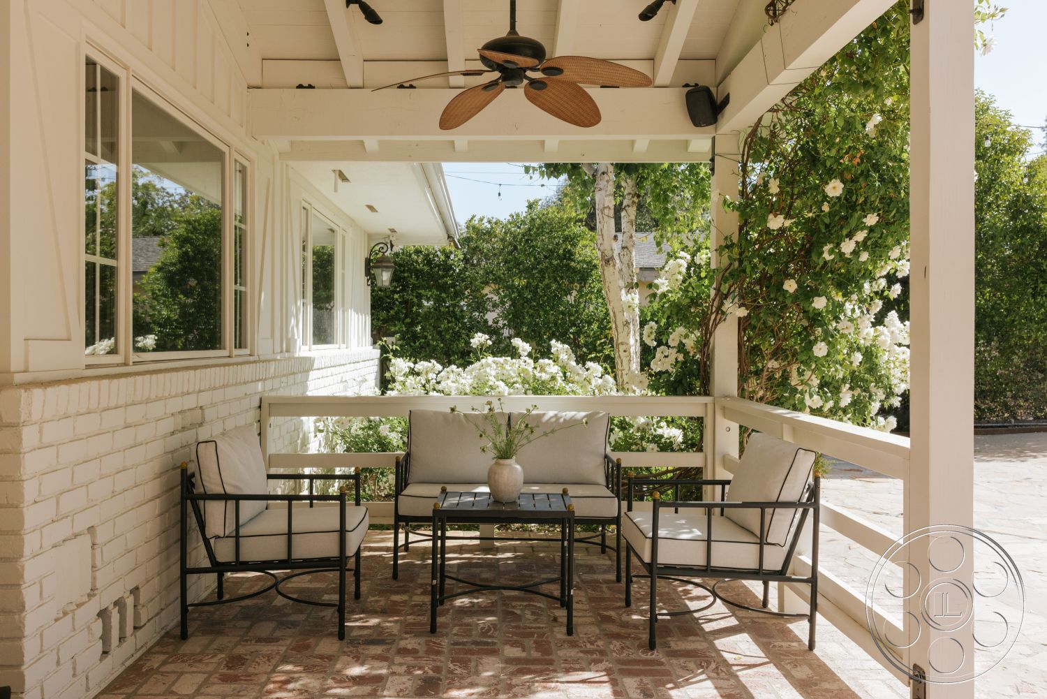 Modern-Farmhouse 20 - exterior, landscaped garden view, metal outdoor furniture, traditional architectural style, exposed wood ceiling beams, white painted walls, brick patio flooring, ceiling fan with wood blades, multitude of white flowering plants, open porch design