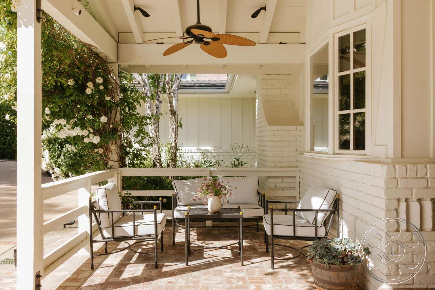 Modern-Farmhouse 20 - natural light, exterior, ceiling fan, covered porch, black metal outdoor furniture, brick patio flooring, decorative potted plant, lush greenery background, white painted brick walls, wooden exposed beams
