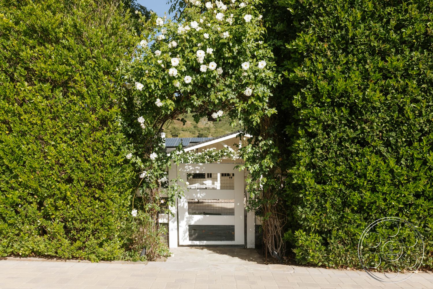 Modern-Farmhouse 20 - exterior, paved driveway, natural greenery, sunlit garden, textured foliage, hedge landscaping, rectangular entrance, white wooden gate, flowering vine arch