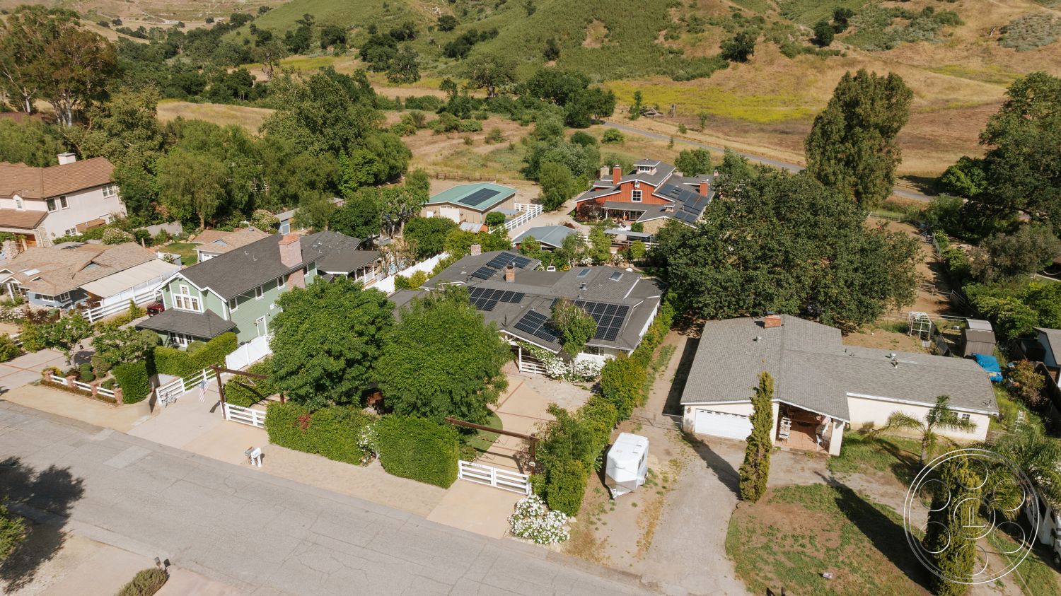 Modern-Farmhouse 20 - exterior, grass lawn, gravel driveway, suburban backyard, wooden fences, solar panels on roof, landscaped garden with shrubs, view of rolling hills, single-story homes, tree-lined setting, low-pitched roofs