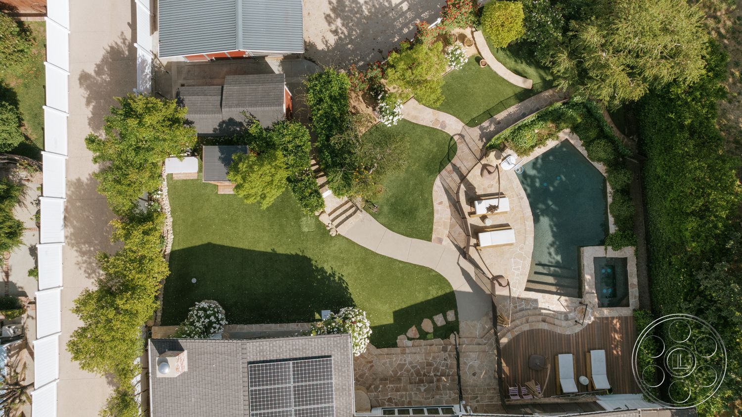 Modern-Farmhouse 20 - exterior, rectangular swimming pool, wooden lounge chairs, modern garden design, circular fire pit, paved stone walkway, landscaped garden beds, solar panels on roof, flagstone pool deck, synthetic grass lawn, surrounding hedges, concrete patio path, built-in spa area, stone garden borders, decorative outdoor plants, sun deck with wooden flooring