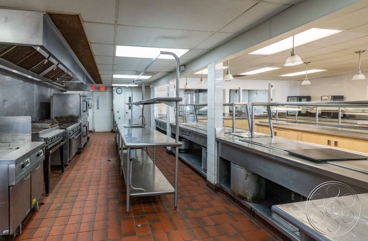 School 1 - high ceilings, tile flooring, open shelving, work tables, bright fluorescent lighting, stainless steel kitchen appliances, interior kitchen, white painted walls, stainless steel countertops, industrial kitchen design, efficient workspace, red clay tile floor, exhaust hood, commercial range, kitchen layout with prep area