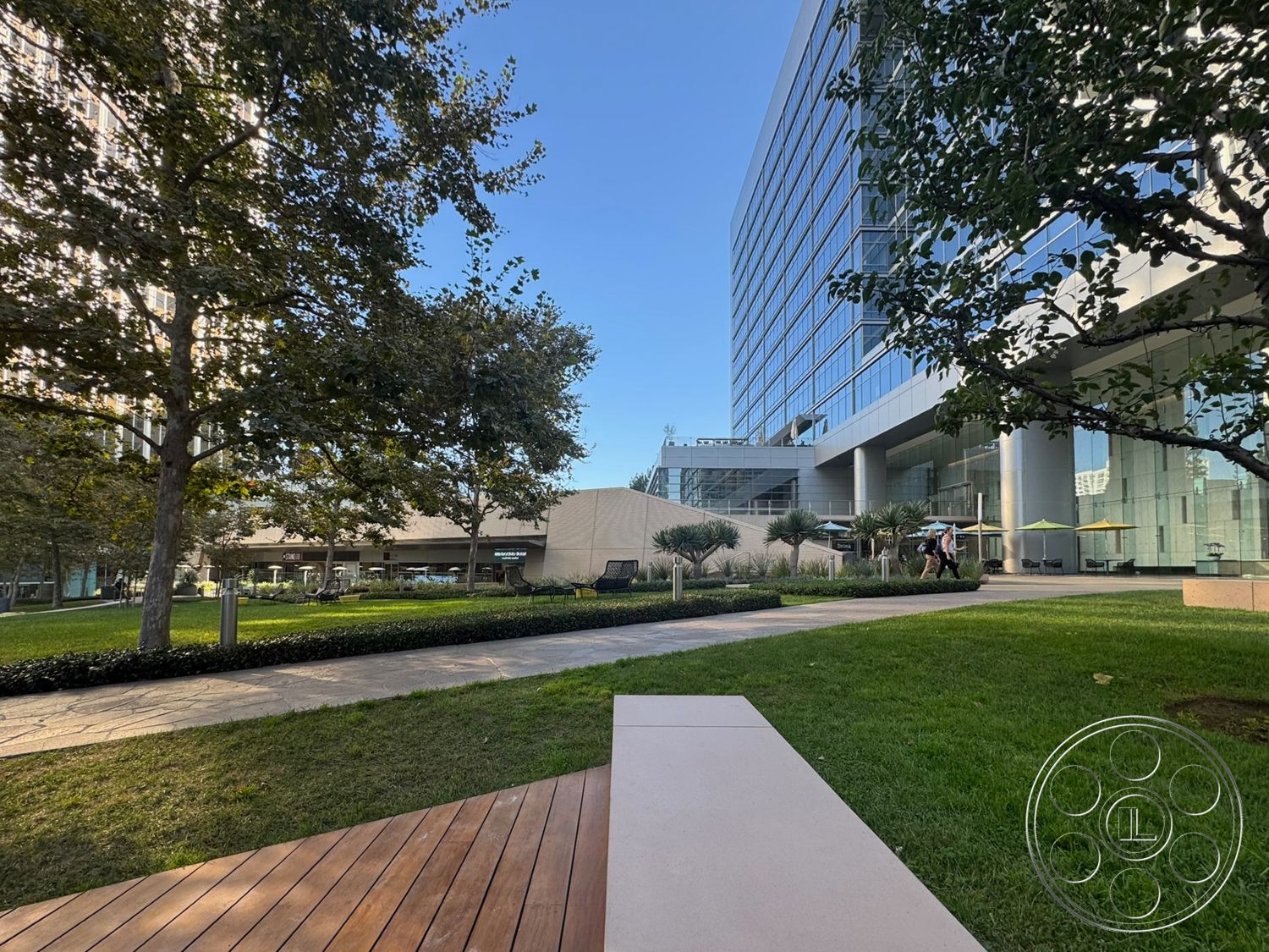 Ave Of The Stars - exterior, wooden bench, outdoor seating area, floor-to-ceiling windows, glass facade, paved pathway, modern architectural style, lawn area, ornamental grasses, urban park setting, concrete building structure, landscaped garden design, metal pathway lighting