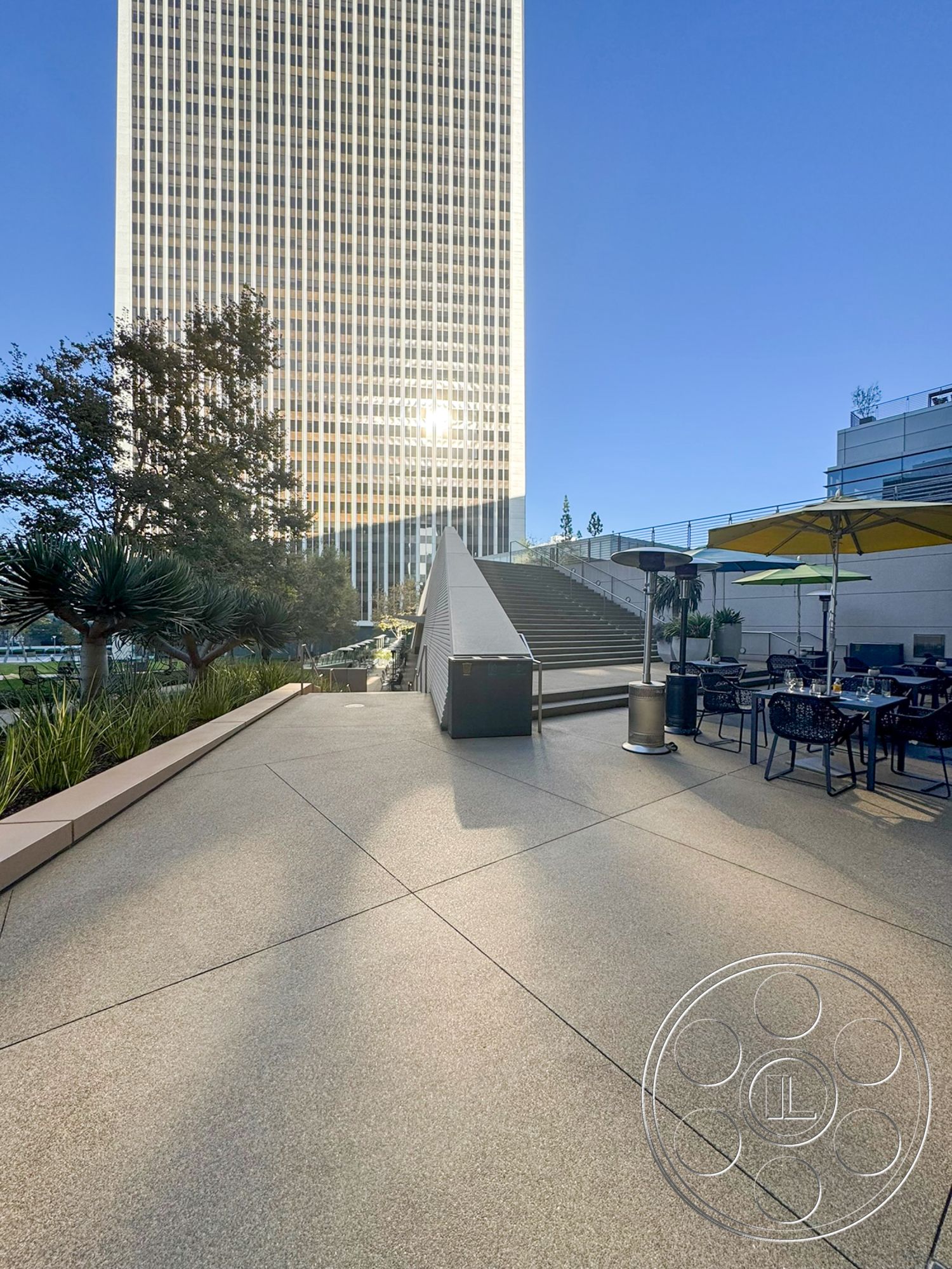 Ave Of The Stars - exterior, metal railing, glass façade, concrete terrace flooring, sunny urban setting, rectangular concrete steps, decorative concrete pathway, modern skyscraper architecture, landscaped greenery with shrubs, patio dining area with tables and chairs, high-rise building backdrop
