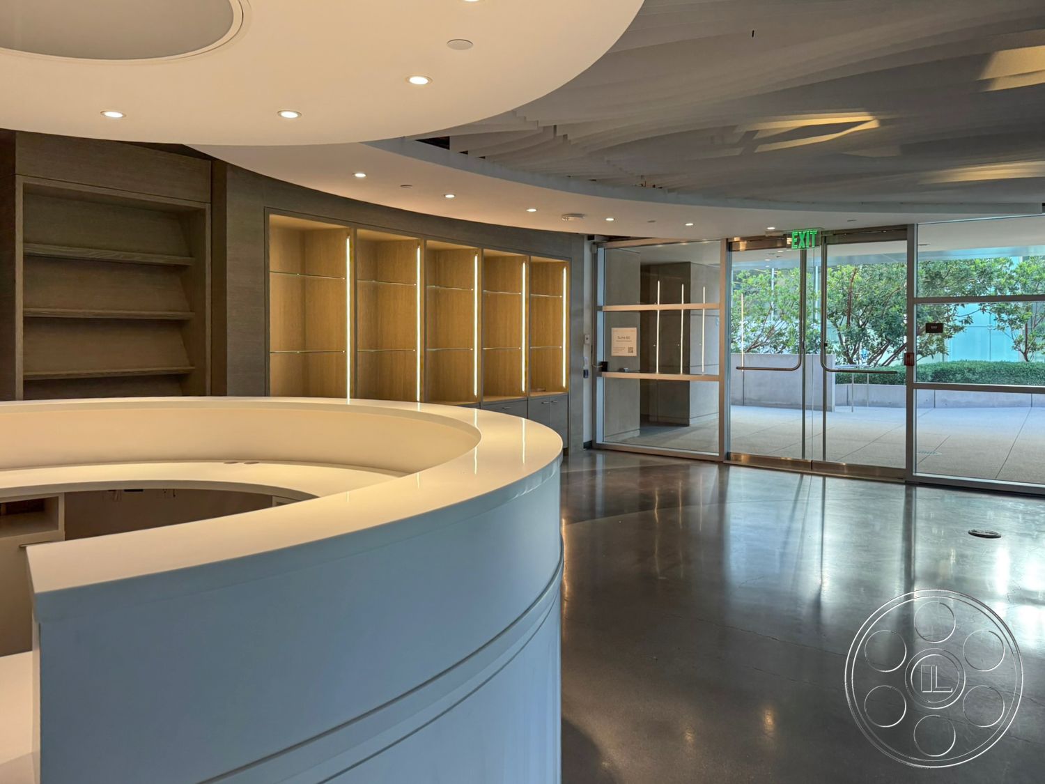 Ave Of The Stars - open layout, polished concrete flooring, modern minimalist design, lush outdoor greenery view, curved white solid surface reception desk, built-in lighted display shelves, soft curved ceiling detail, floor-to-ceiling glass entrance doors, wood accent wall with warm lighting
