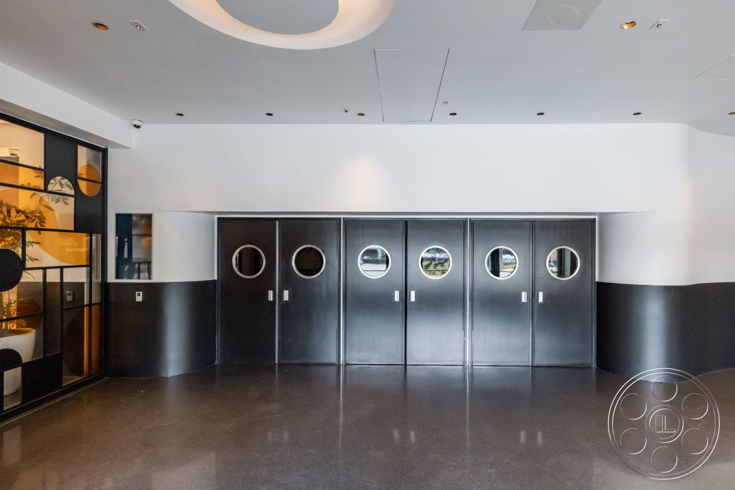Sunset Campus - polished concrete flooring, modern architectural style, white painted walls, curved ceiling design, black panel doors with circular windows, geometric glass partition with black and yellow accents