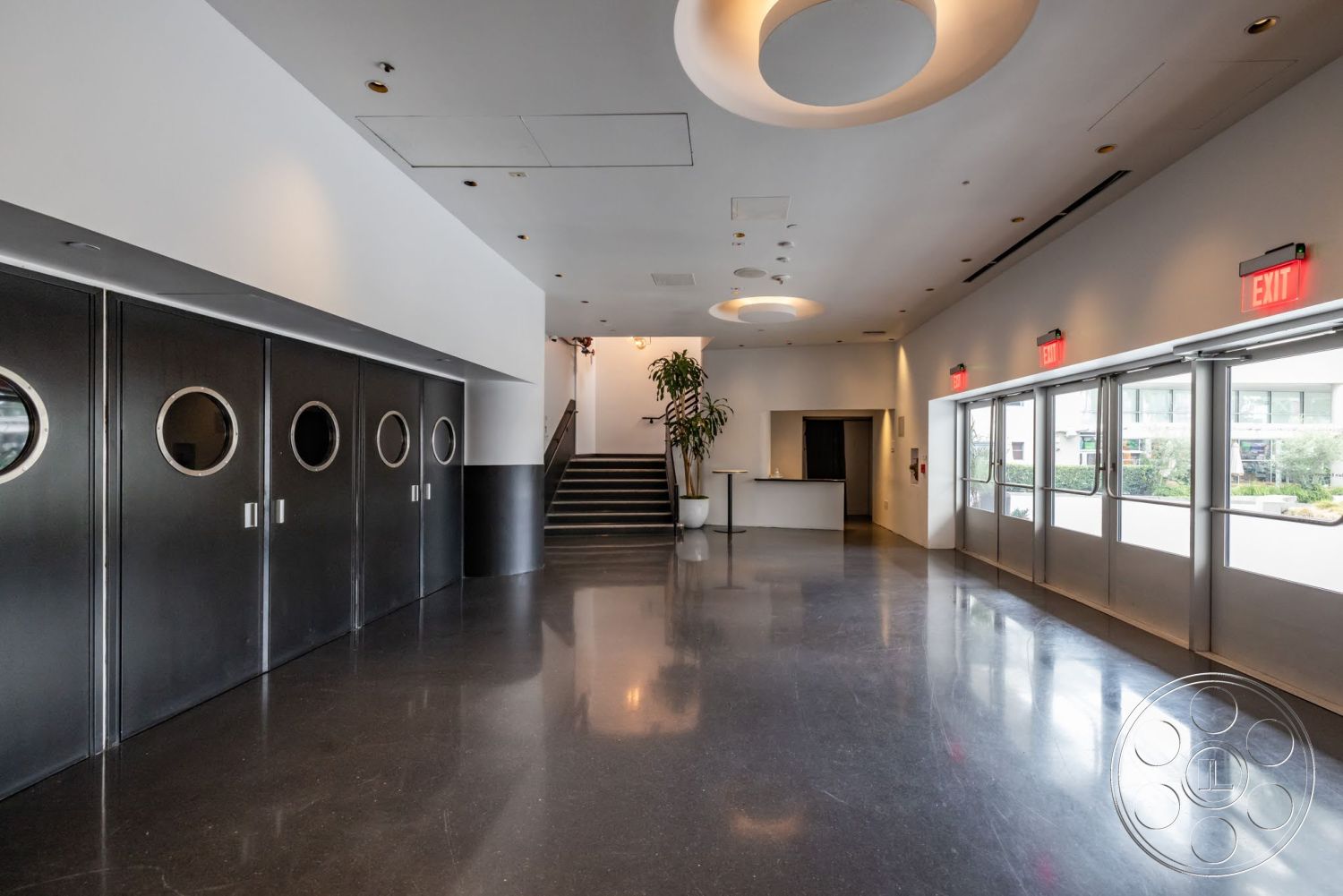 Sunset Campus - polished concrete flooring, floor-to-ceiling windows, recessed ceiling lighting, modern minimalist design, white painted walls, stainless steel handrail, circular ceiling light fixture, black metal doors with circular windows, open layout entrance hall