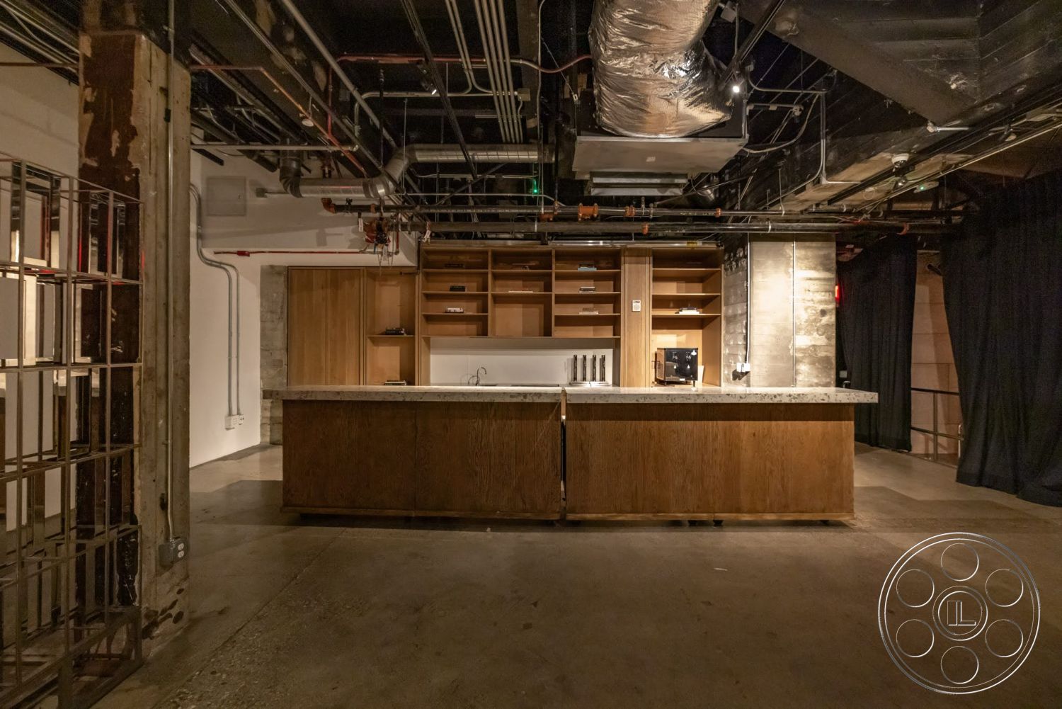 Sunset Campus - polished concrete floor, wood cabinetry, exposed concrete walls, glass partition, metal piping, modern kitchen design, granite kitchen countertop, open shelving units, industrial ceiling with exposed ductwork, dark fabric curtains