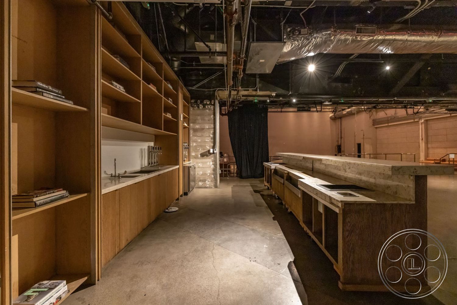 Sunset Campus - spacious layout, minimalist design, concrete floor, ambient lighting, concrete countertop, modern style, exposed ductwork ceiling, industrial interior, wood shelving units, built-in bar area, dark curtain partition
