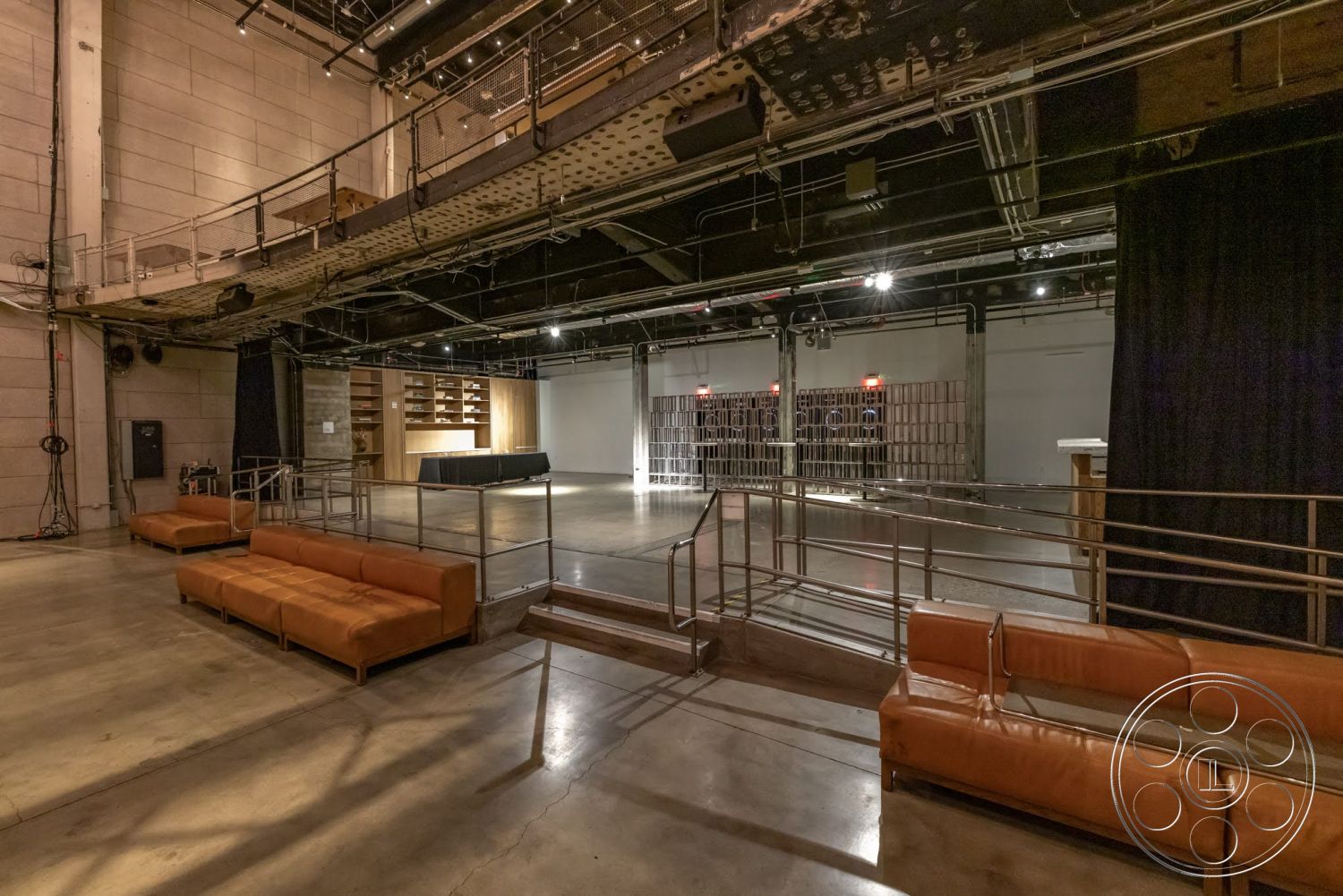 Sunset Campus - open floor plan, polished concrete flooring, exposed concrete walls, industrial lighting fixtures, wood shelving units, metal railing detail, orange leather sofas