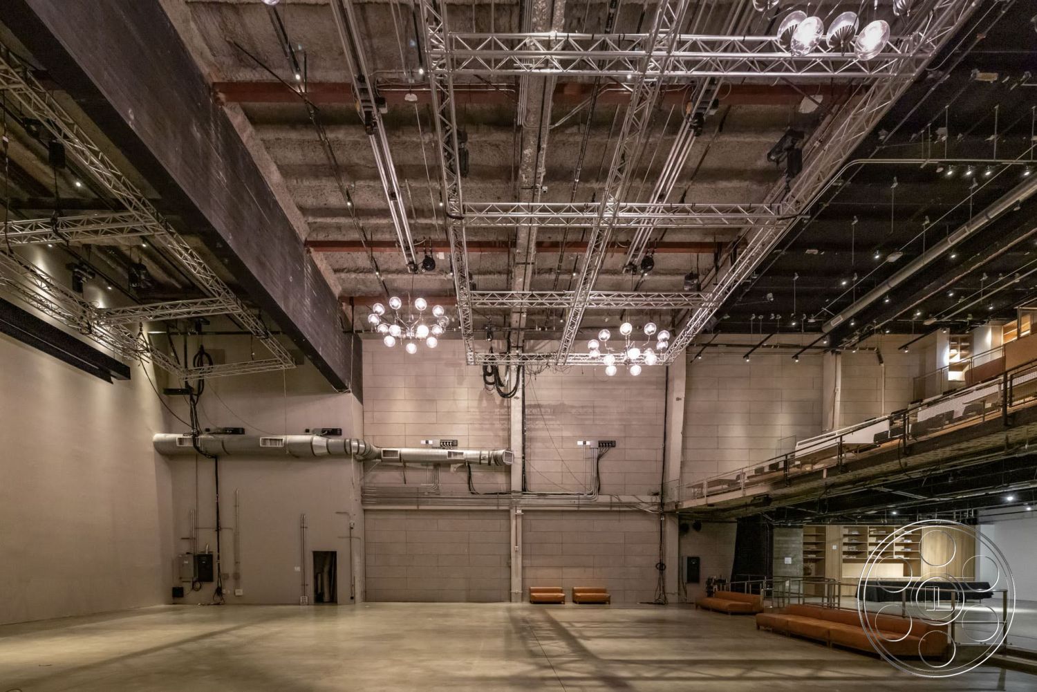 Sunset Campus - neutral color palette, concrete flooring, exposed concrete walls, mix of textures, suspended light fixtures, modern architectural details, industrial-style lighting, wide open space layout, metal truss ceiling, glossy floor finish, theater room design