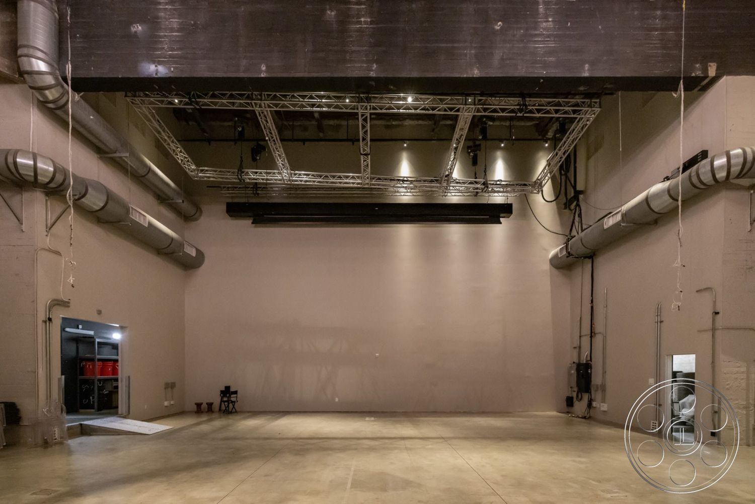 Sunset Campus - concrete flooring, open space layout, exposed ductwork, structural support beams, white painted walls, black painted ceiling, interior warehouse space, industrial ceiling lights, drywall walls, loading dock entrance, steel truss ceiling