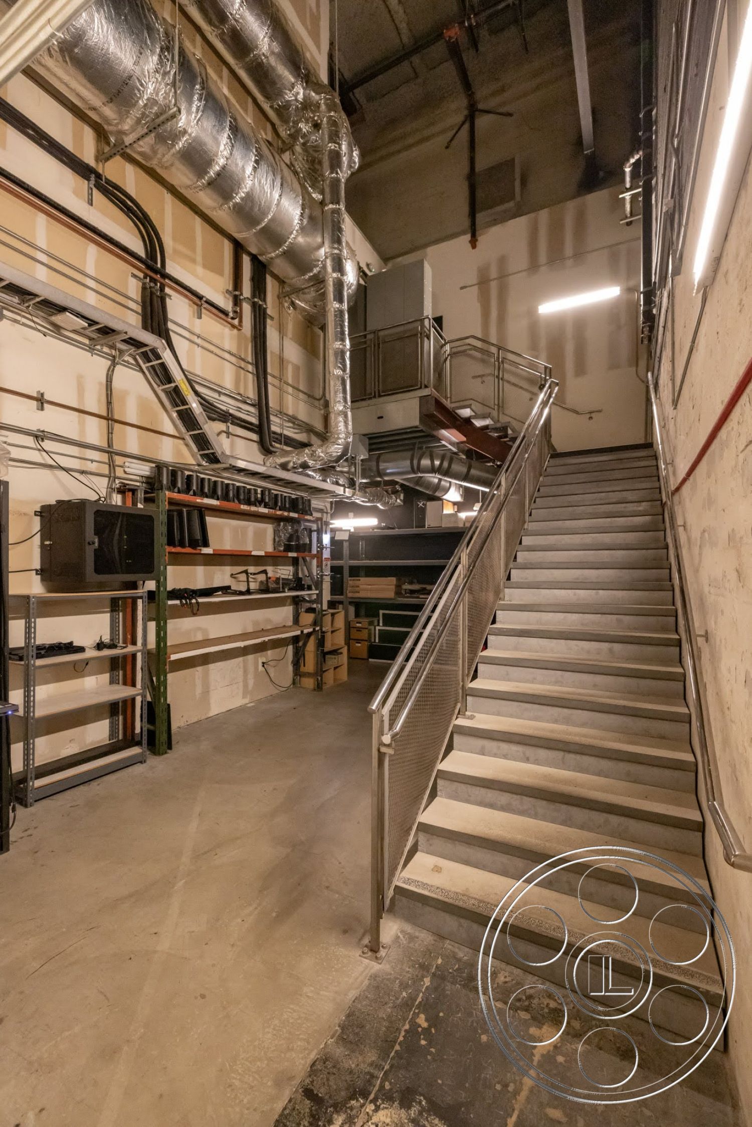 Sunset Campus - open shelving, exposed concrete flooring, metal stair railing, concrete staircase, ambient LED strip lighting, industrial-style exposed ductwork, galvanized steel support beams, painted sheetrock walls, utility room setting