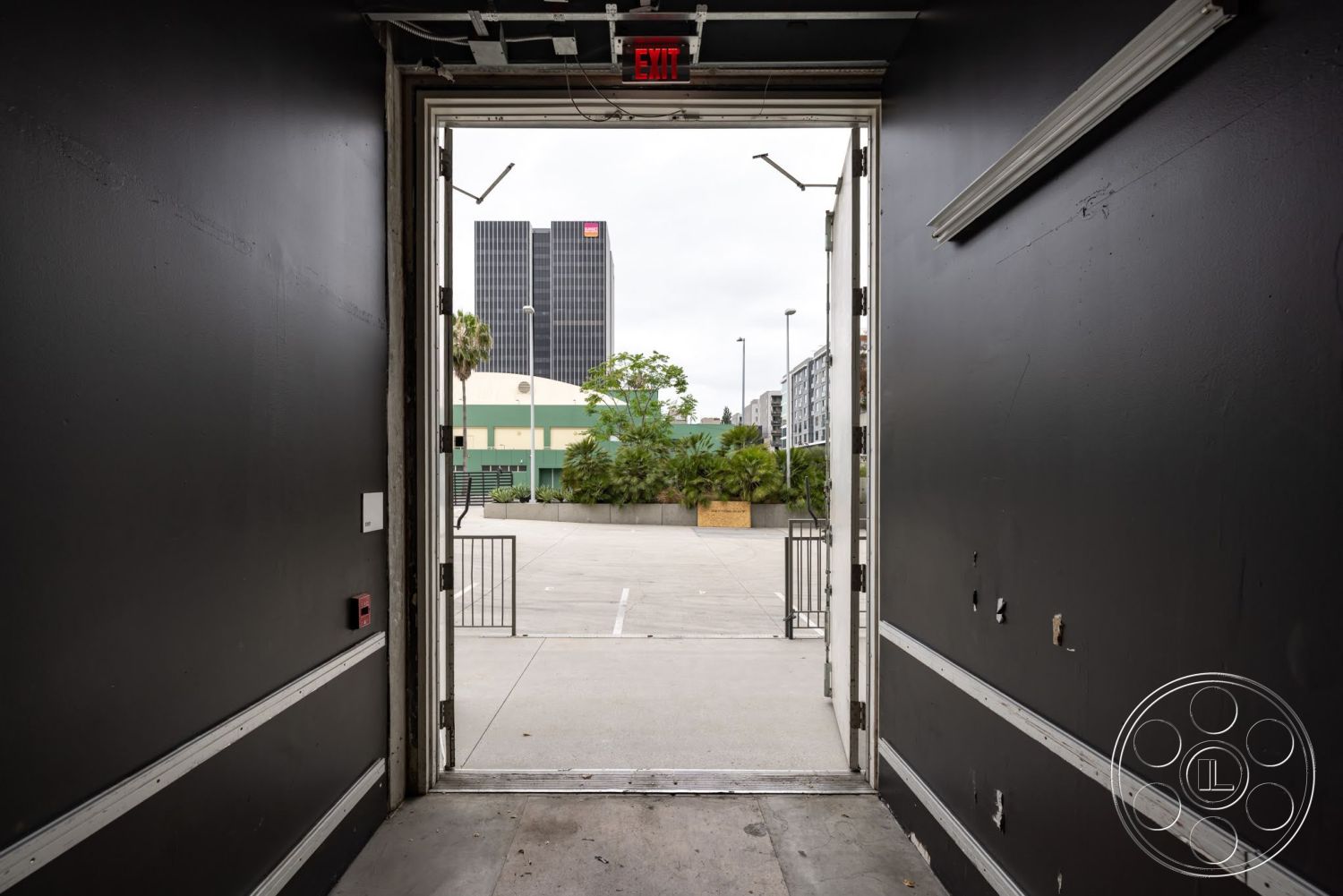 Sunset Campus - exterior, concrete floor, urban environment, city skyline view, black painted walls, modern architectural details, metal door frame, floor-to-ceiling doorway, security exit sign, open doorway leading to outdoor area