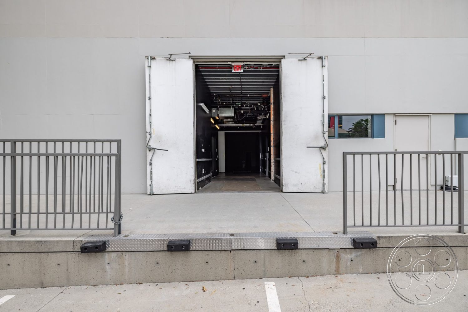 Sunset Campus - metal railing, gray concrete walls, minimalist architectural design, flat roof structure, exterior concrete loading dock, large double doors, industrial entryway, open loading area, steel door frames, paved concrete ground