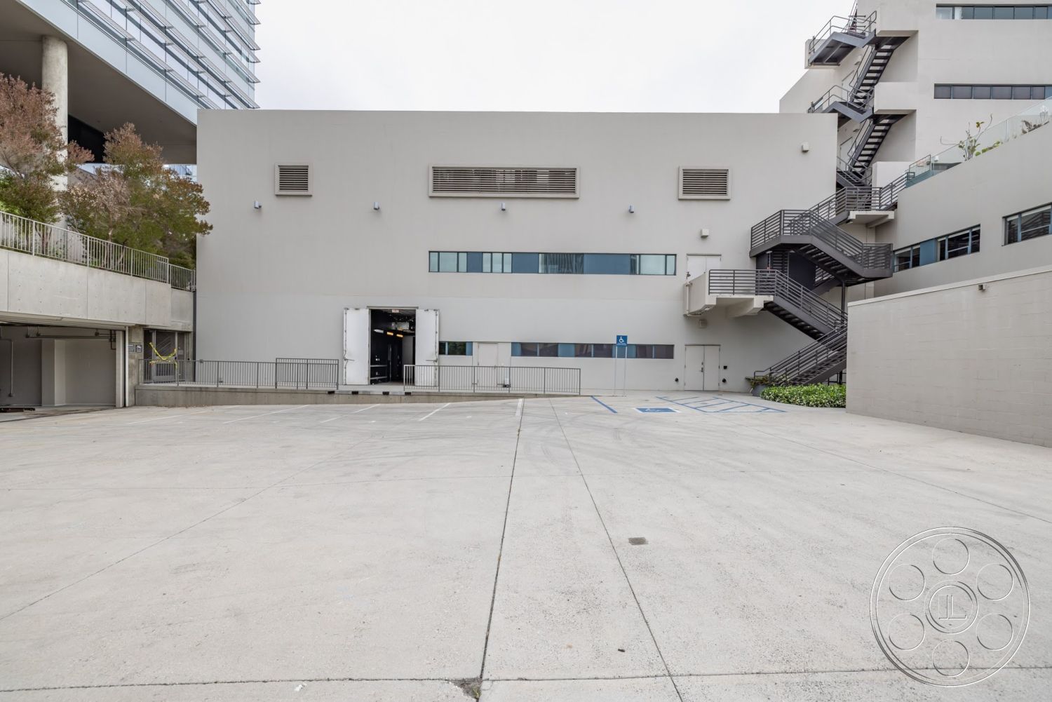Sunset Campus - exterior, urban setting, glass windows, industrial architecture, gray stucco walls, concrete parking lot, flat roof design, commercial building facade, metal fire escape stairs, sidewalk with railings