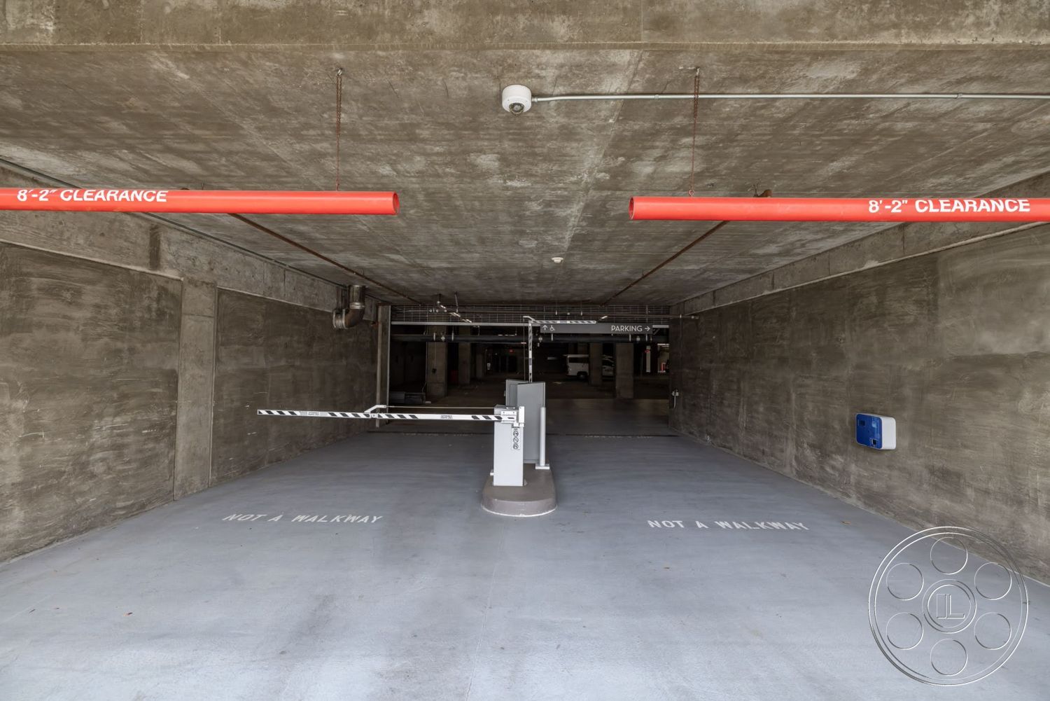 Sunset Campus - exposed concrete walls, concrete garage floor, ceiling-mounted lighting fixtures, red clearance signage, metal parking barrier, industrial parking structure, floor markings for pedestrian guidance, open parking space layout