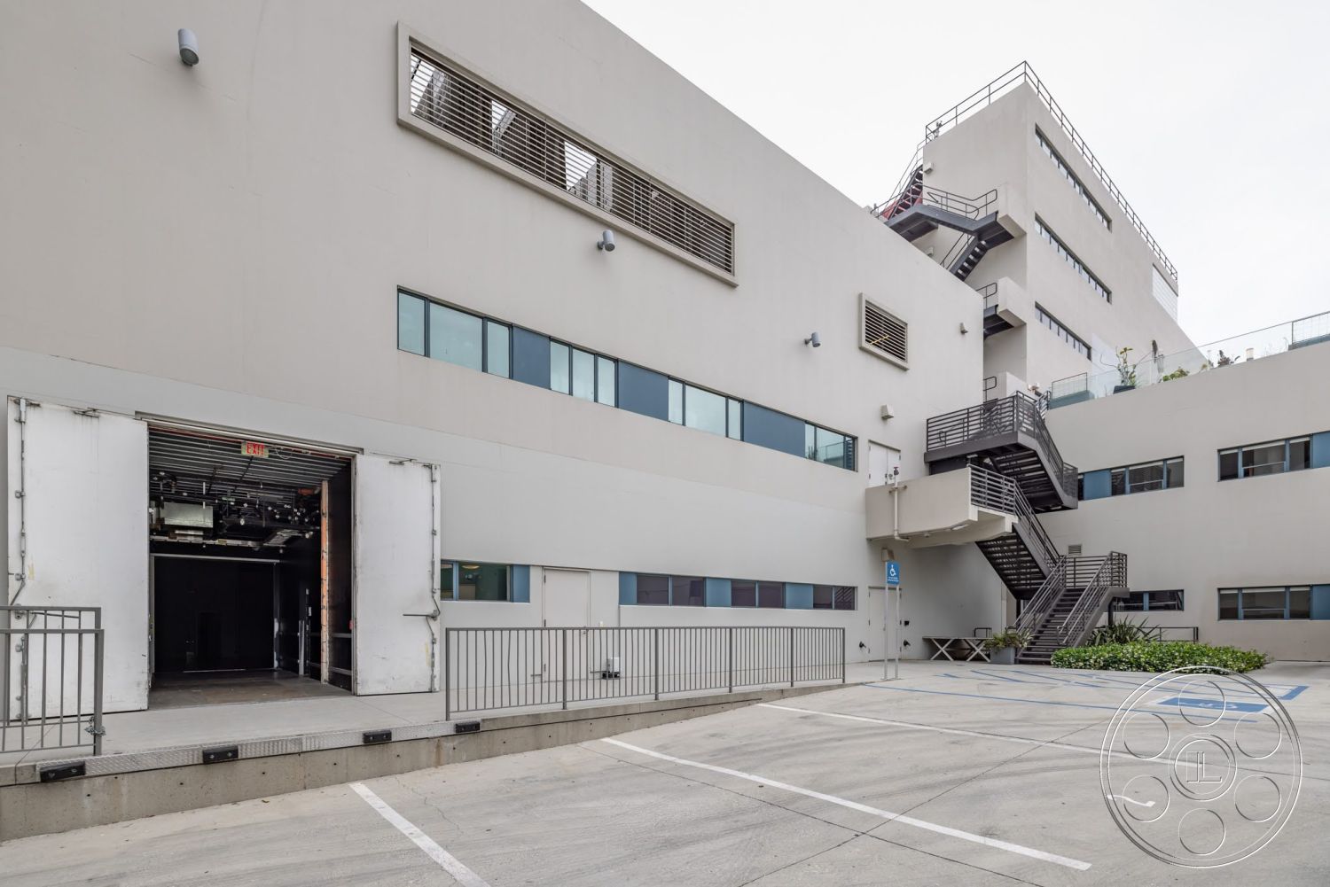 Sunset Campus - exterior, landscaped greenery, loading dock access, flat roof design, aluminum window frames, concrete exterior walls, modern architectural details, industrial-style architecture, metal stair railing, concrete parking area, large window panels, corrugated metal accents, steel fire escape staircase
