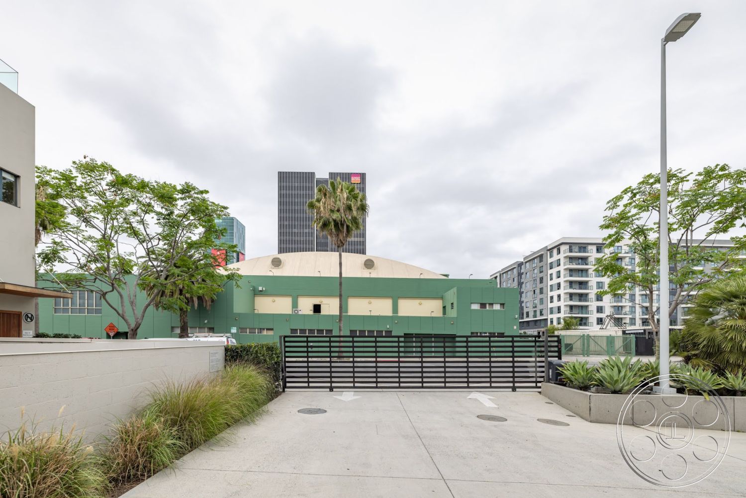Sunset Campus - exterior, commercial building, concrete planters, modern architectural style, concrete driveway, mixed-use development, flat roof structure, surrounding urban environment, green painted building facade, metal gated entrance, landscaped plants with palms, two-story commercial complex