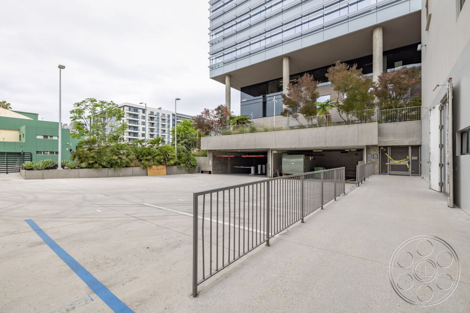 Sunset Campus - exterior, paved driveway, urban setting, modern architectural style, concrete parking lot, concrete retaining wall, landscaped garden area, glass curtain wall, exposed concrete pillars, steel railing fence