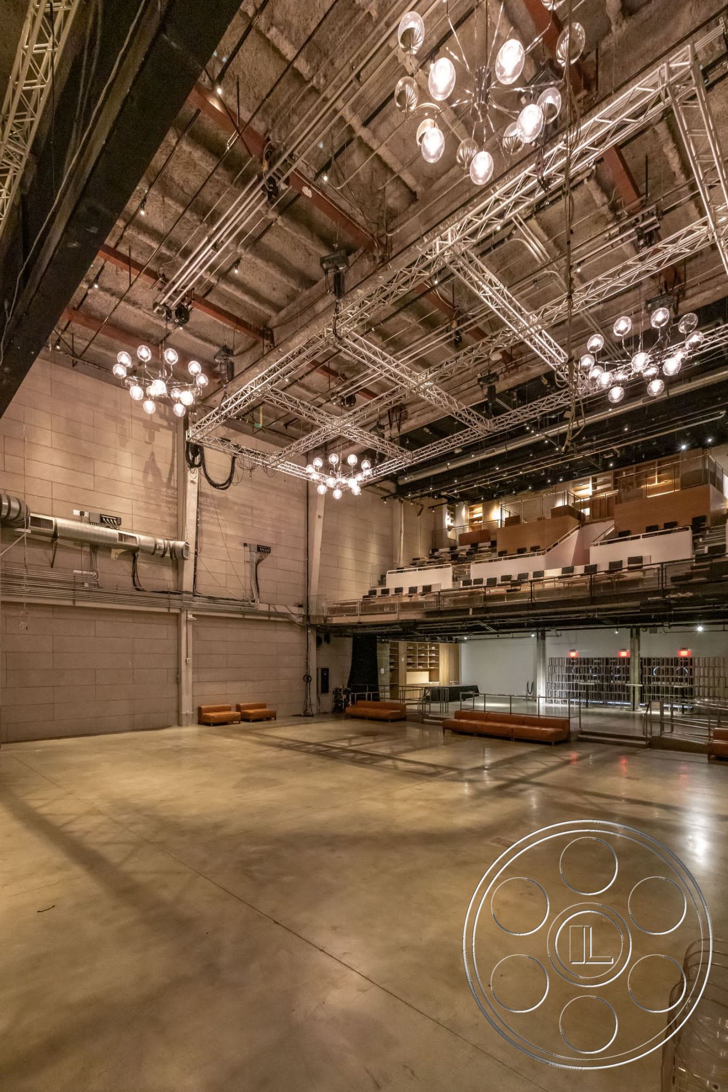 Sunset Campus - concrete block walls, industrial lighting fixtures, exposed concrete flooring, open performance space, metal ceiling beams, modern auditorium design, tiered seating area, steel grid support structure