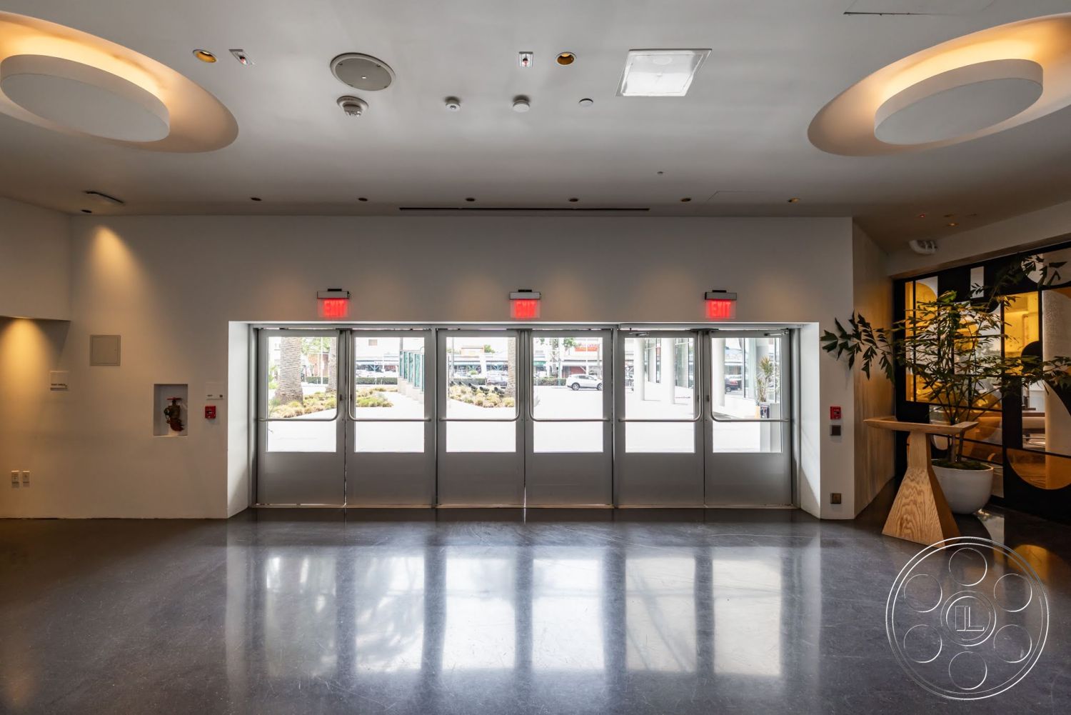 Sunset Campus - minimalist design, polished concrete flooring, planter with greenery, open entryway, wood accent table, modern ceiling lights, textured white walls, fire safety equipment, frosted glass entrance doors