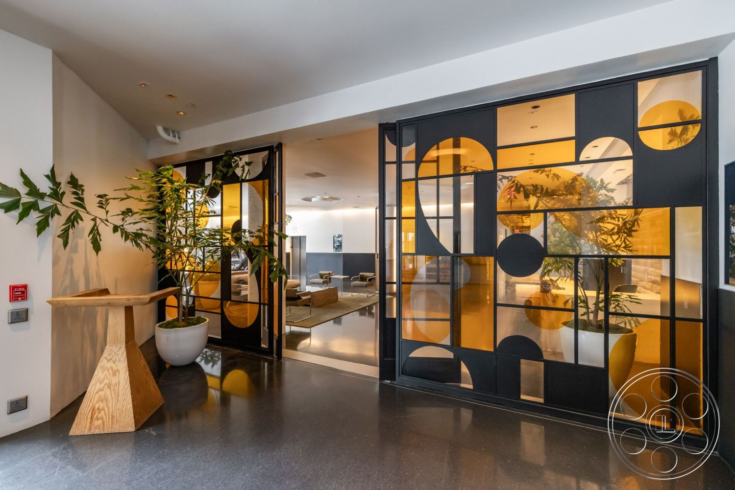 Sunset Campus - modern architecture, minimalist design, open floor plan, polished concrete flooring, warm ambient lighting, wood accent table, contemporary entryway, large potted plant, black metal framed glass doors, geometric glass inserts, yellow-tinted glass panels