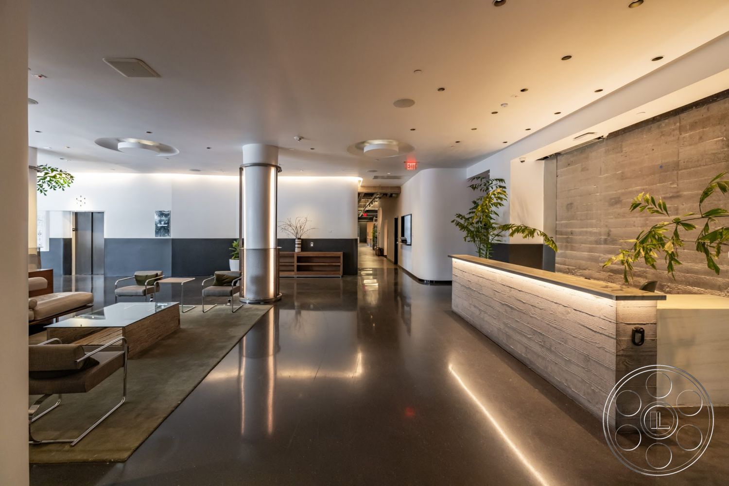 Sunset Campus - greenery accents, polished concrete flooring, glass coffee table, exposed concrete wall, wood accent wall, modern lounge seating, linear recessed lighting, minimalist reception desk, sleek metallic column, dark wall paneling, low-profile area rug