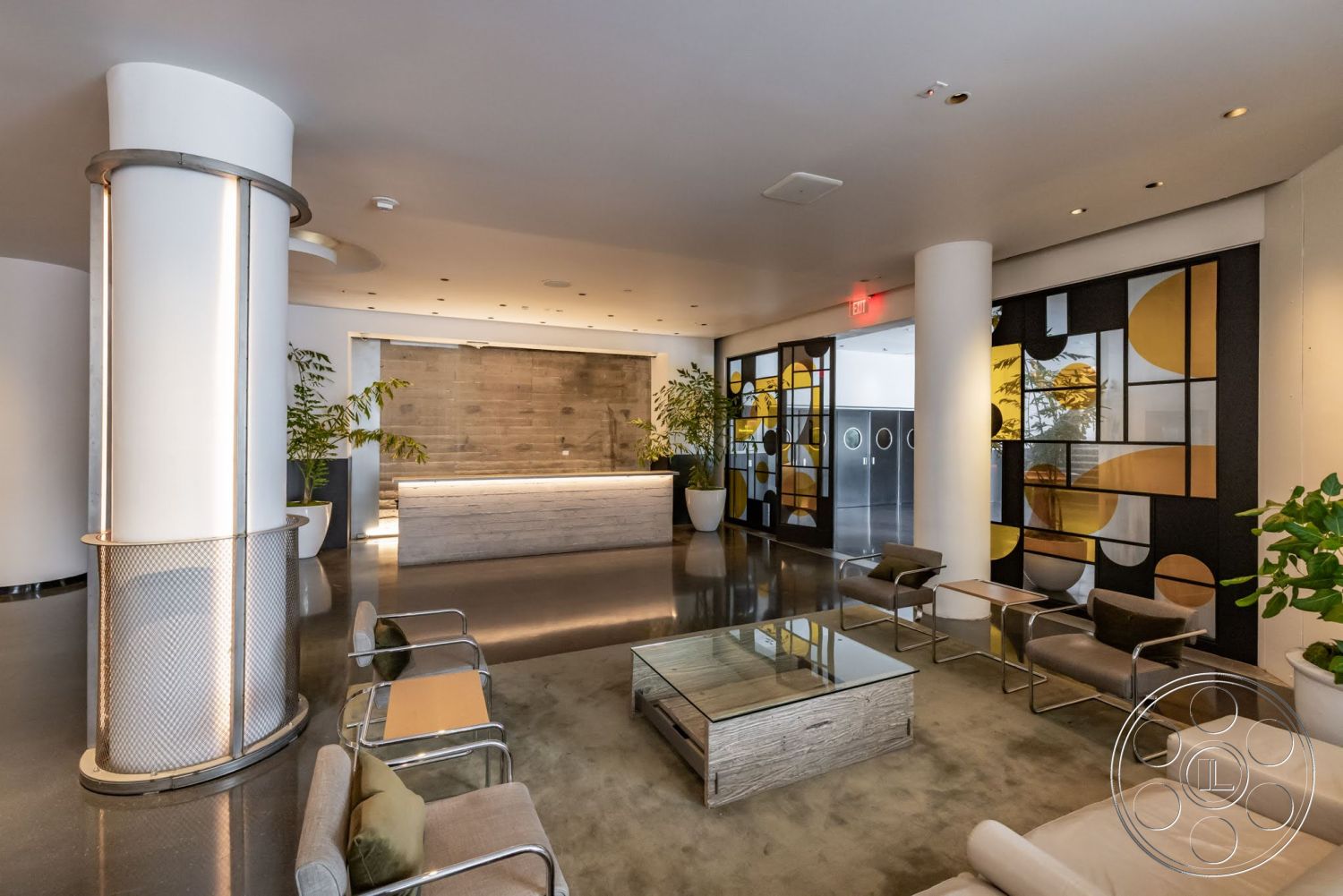 Sunset Campus - polished concrete floor, exposed concrete wall, minimalist coffee table, potted indoor plants, ambient ceiling lighting, metal-framed chairs, light wooden reception desk, glass panel wall with geometric patterns, circular metal columns